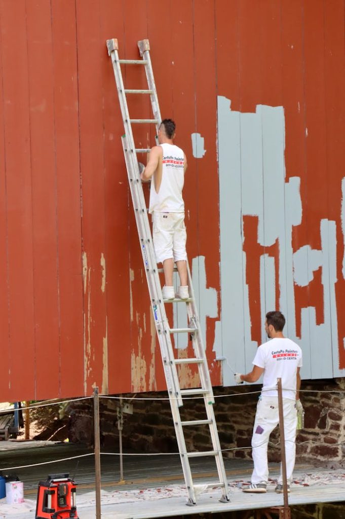 Two men repainting a large wall using a ladder, engaged in renovation work outdoors.